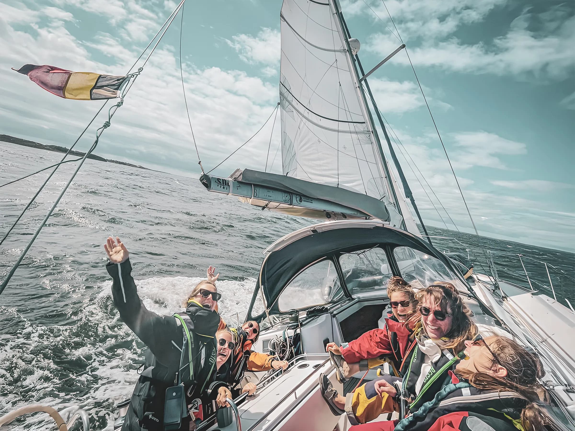 Groupe souriant en voilier sur les eaux du Pays de Galle, paysages marins captivants.