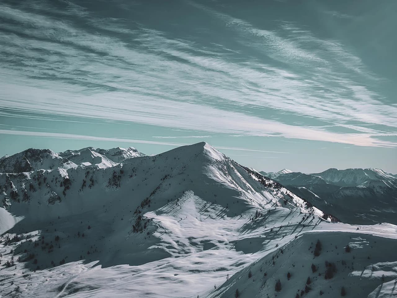 Paysage alpin enneigé, sommets majestueux sous un ciel lumineux, invitation à l'aventure hivernale.