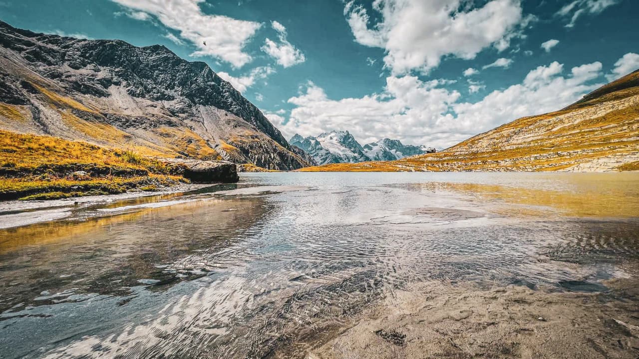 Calme lac alpin aux reflets scintillants, entouré de montagnes majestueuses sous un ciel ensoleillé.