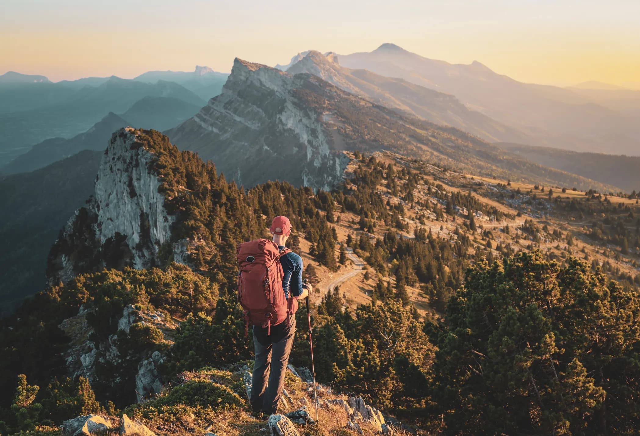 Randonneur contemplant un paysage montagneux à la lumière dorée du coucher de soleil.