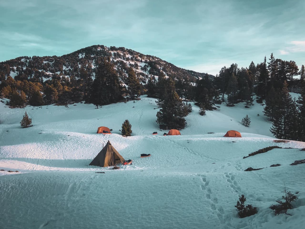 Wonderful winter landscape with tipis and orange tents, surrounded by snow and majestic mountains.