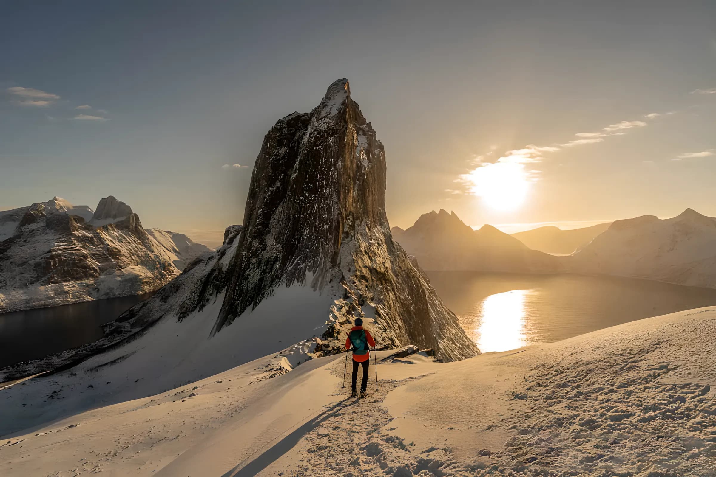 A hiker contemplating a snow-covered landscape at sunset on the island of Senja in Norway.