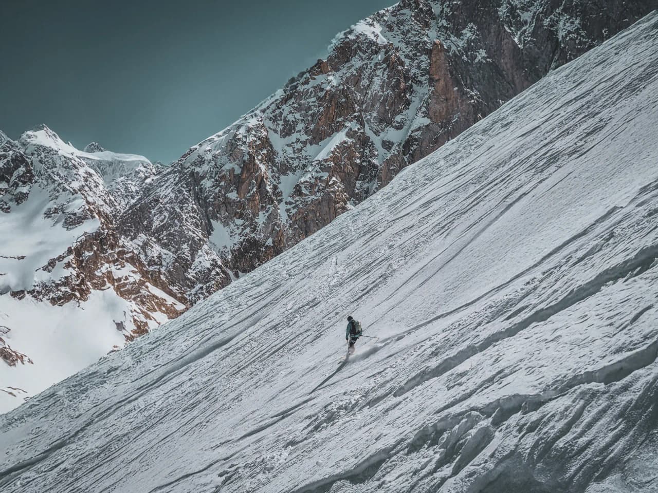 Un skieur solitaire descend un versant enneigé, entouré de majestueuses montagnes alpines.