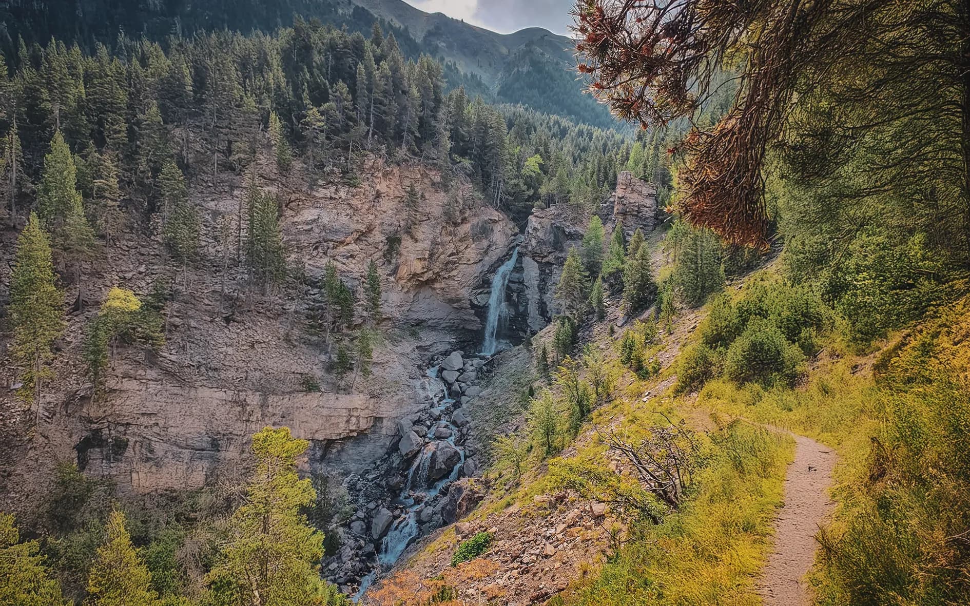 A leafy path leading to a picturesque waterfall, surrounded by majestic mountains.