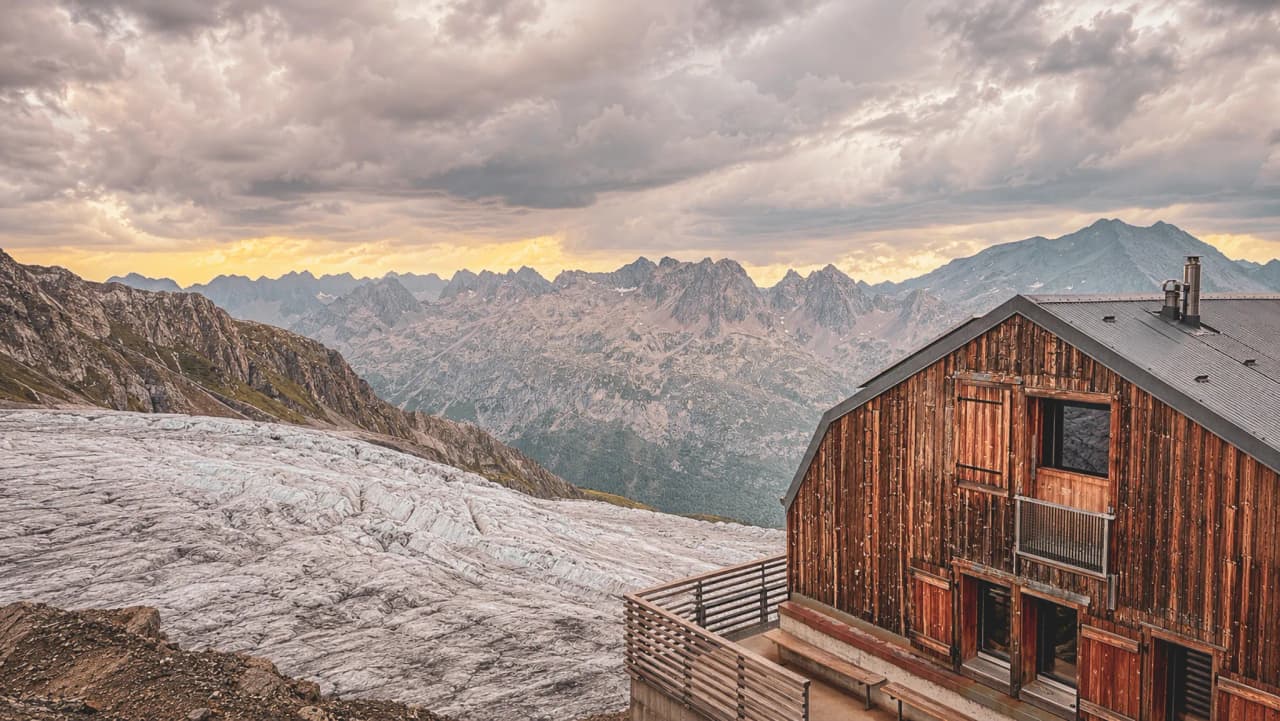 Magnifique paysage alpin avec un chalet en bois surplombant un glacier et des montagnes majestueuses.