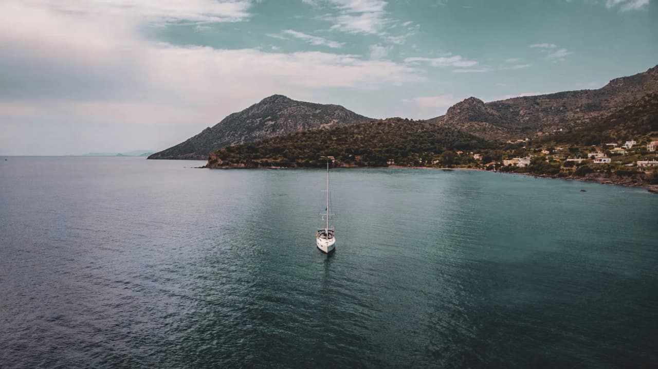 Un voilier glissant sur des eaux turquoise, entouré de collines verdoyantes en Grèce.