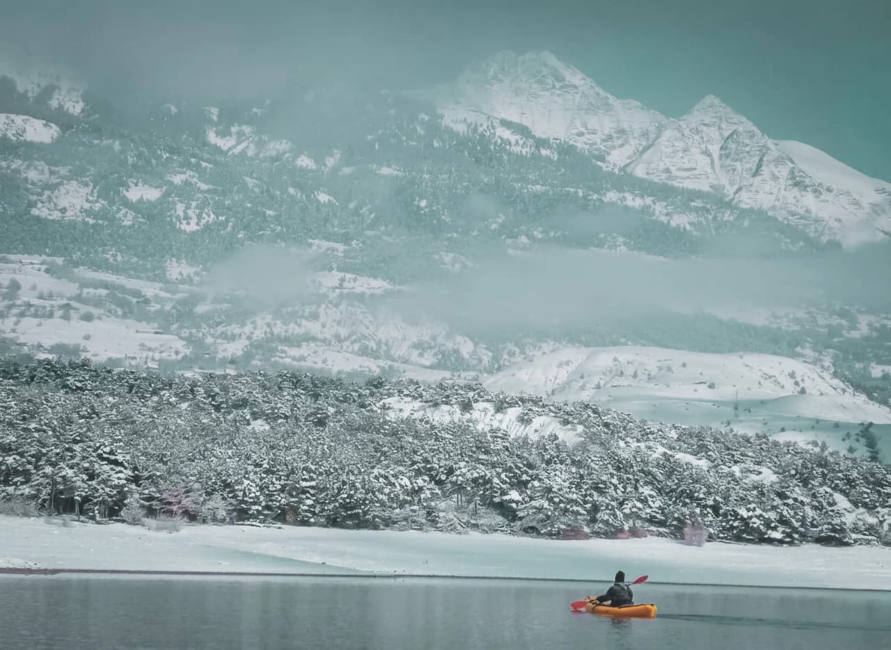 Un kayakiste glisse paisiblement sur le lac gelé, entouré de montagnes enneigées.