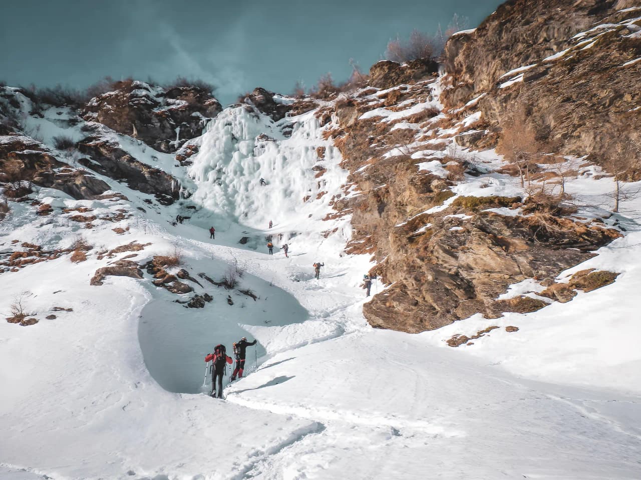 Groupe d'aventuriers s'initiant à la cascade de glace dans un paysage alpin enneigé.