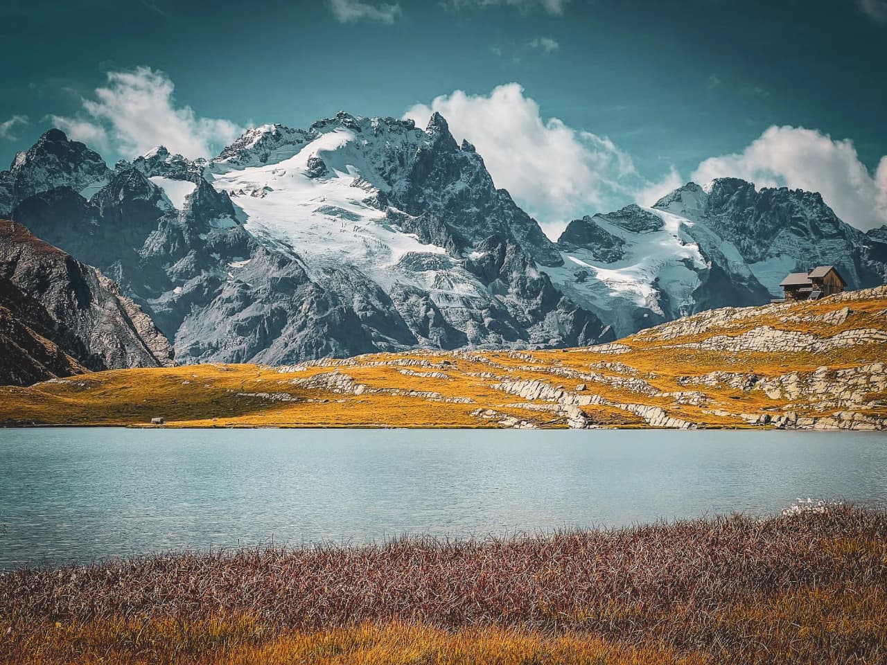 Lac turquoise entouré de montagnes majestueuses sous un ciel ensoleillé, invitation à l'évasion alpine.