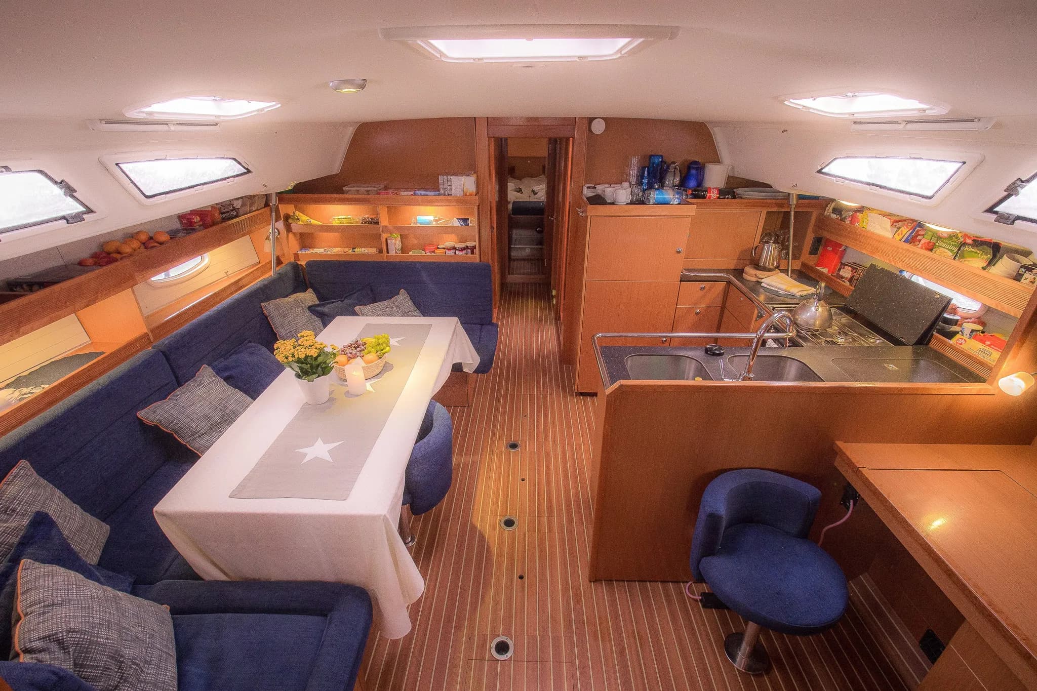 Un intérieur de yacht avec un agencement confortable et fonctionnel. Des canapés bleu foncé entourent une table de salle à manger. La table est ornée d'un chemin de table gris avec une étoile blanche et un vase de fleurs