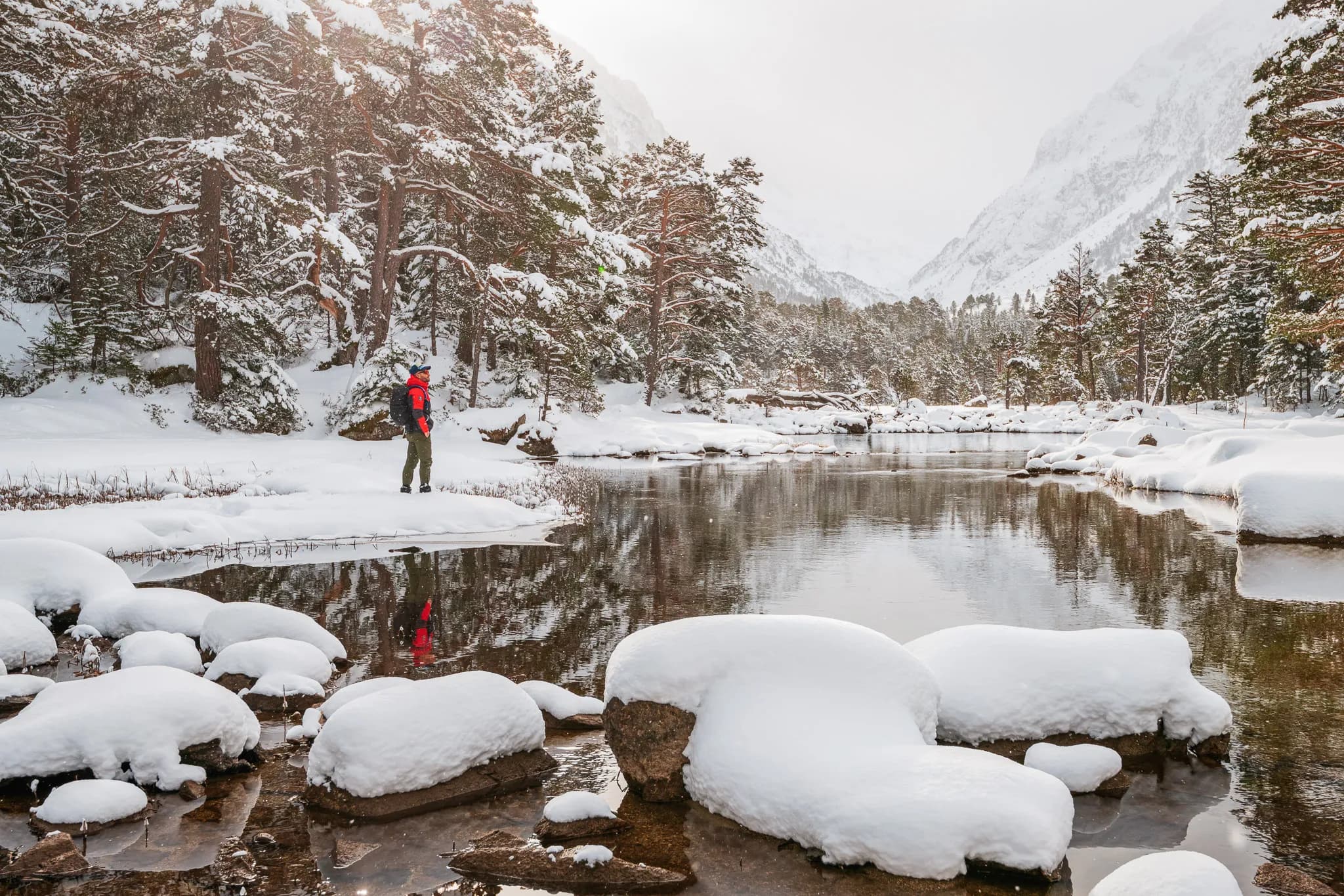 Snowshoe hiker in a snow-covered Pyrenees landscape, reflection on the peaceful water.