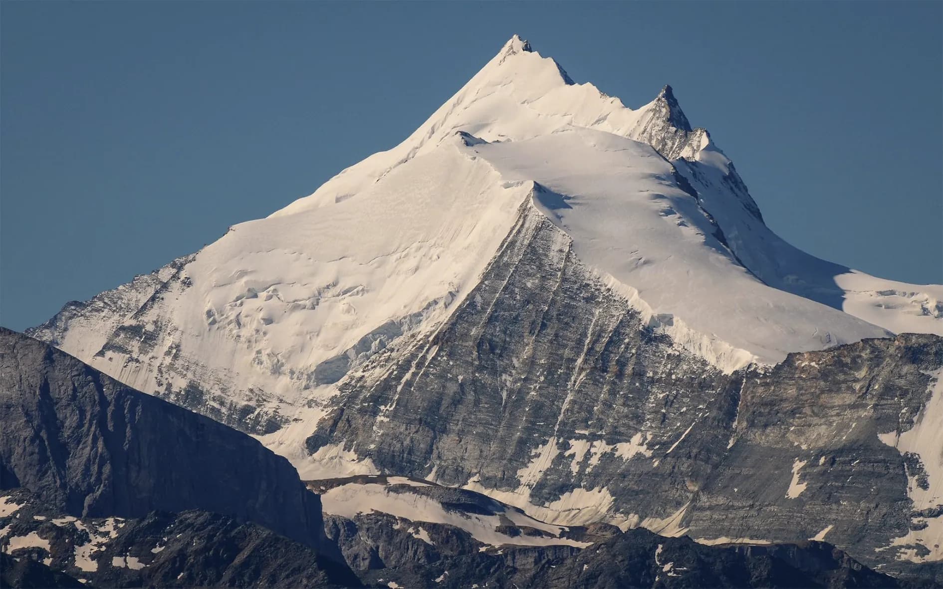 A steep mountain peak, covered in snow and ice, rises majestically beneath a clear blue sky.