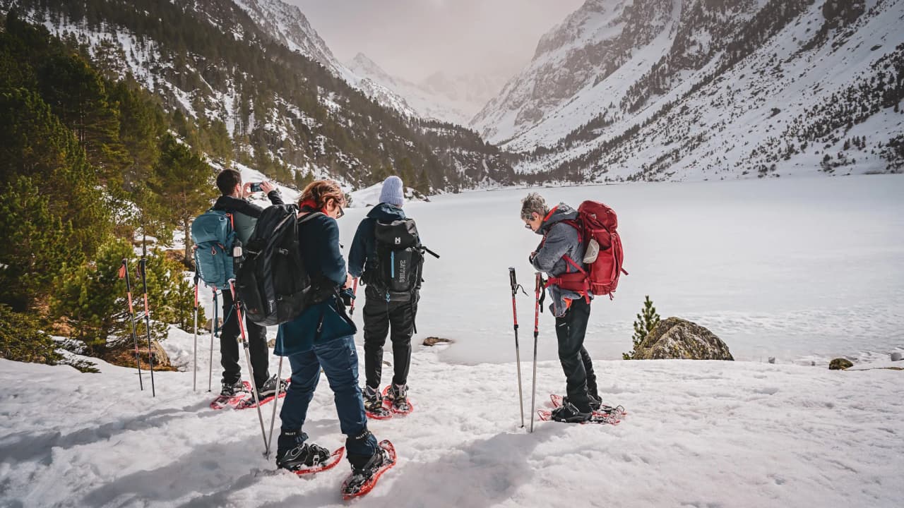A group of hikers on snowshoes in front of a frozen lake, surrounded by snow-capped mountains.