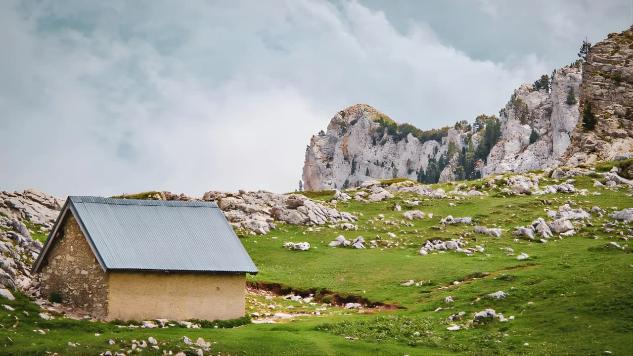 Une charmante cabane en pierre, entourée de prairies verdoyantes et de majestueuses montagnes.