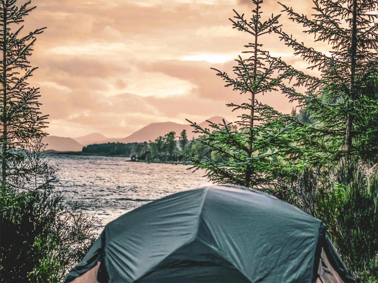 Tent aan de rand van een loch, bergen op de achtergrond onder een gouden hemel, een uitnodiging voor Schots avontuur.