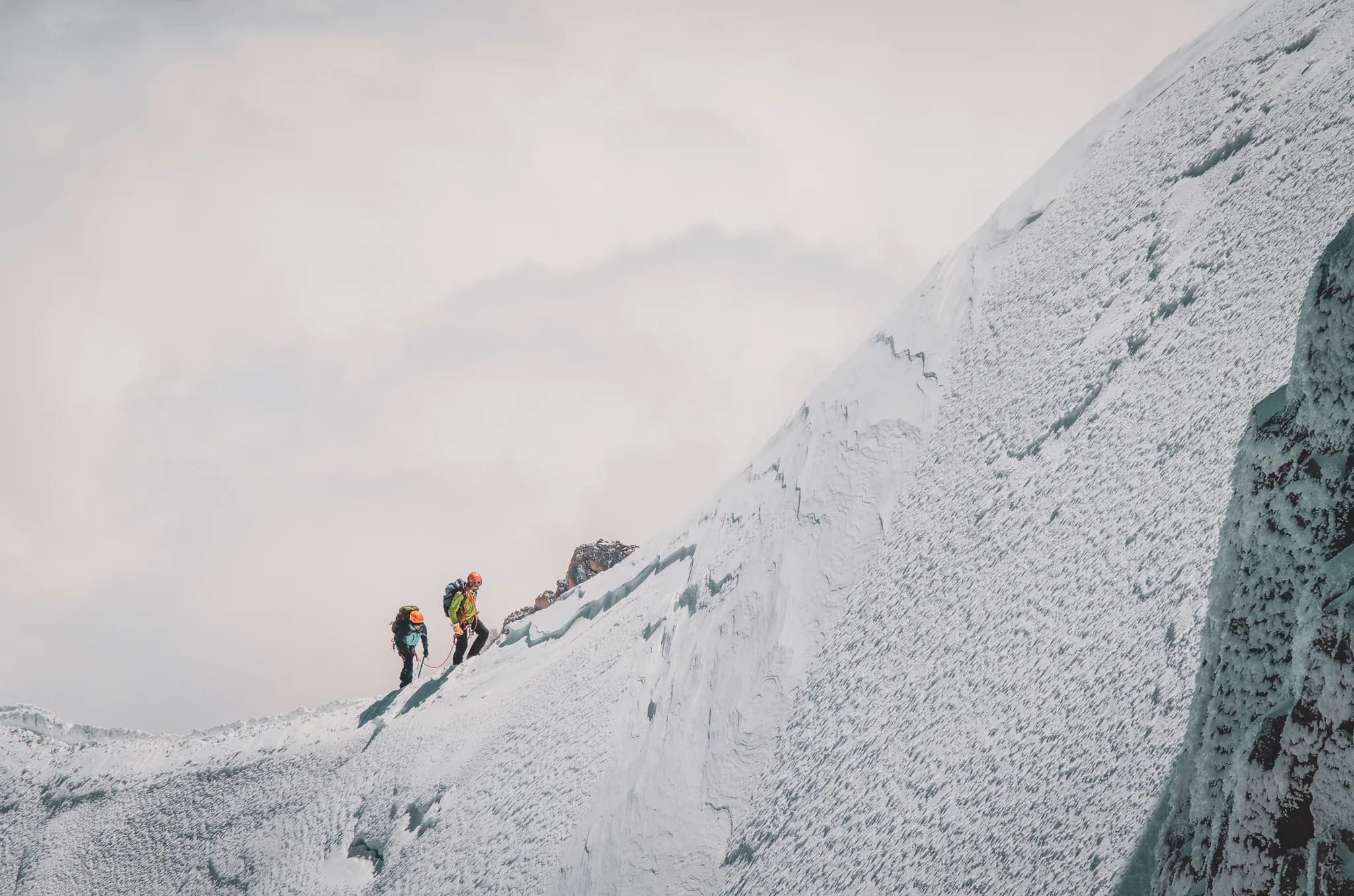 Deux alpinistes grimpent un glacier sur le Mont Blanc, sous un ciel nuageux et majestueux.