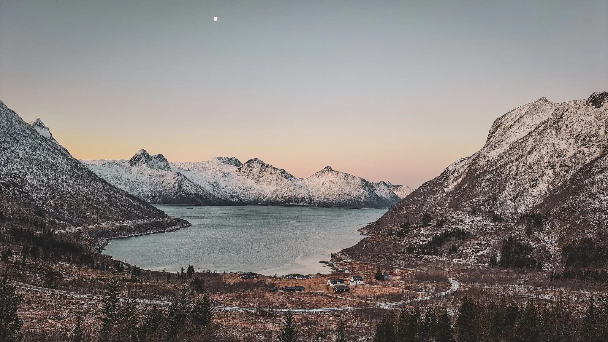 Magnificent panorama of the Senja fjords, Norway, surrounded by snow-capped mountains at dusk.