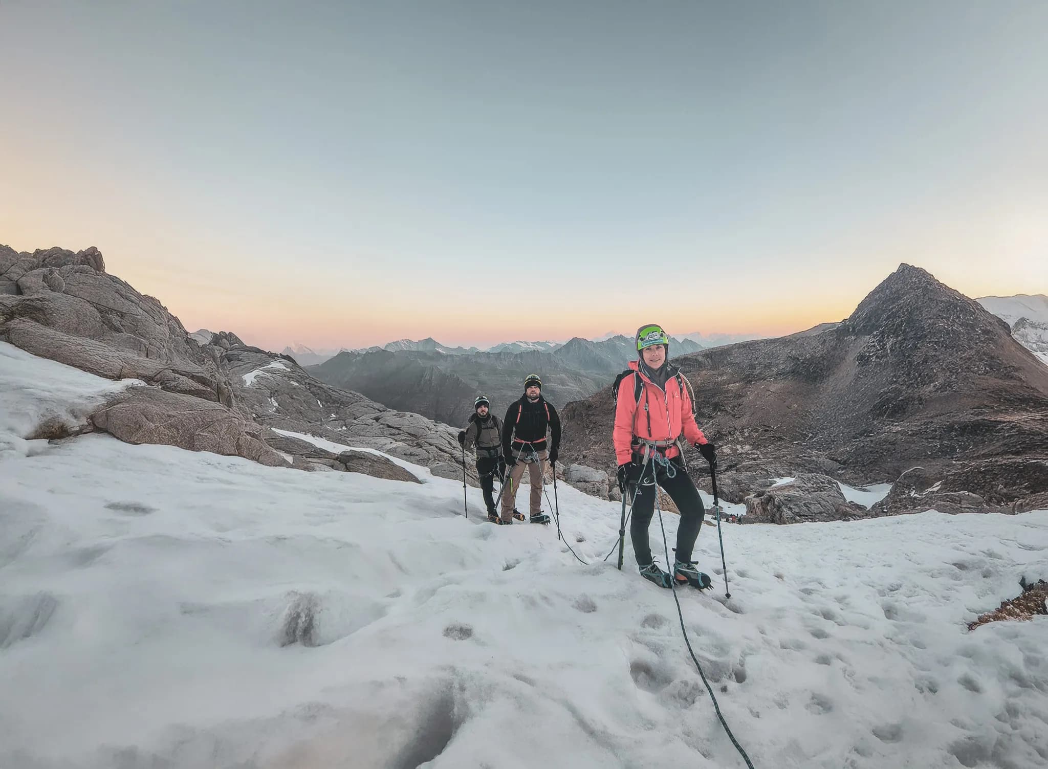 A group of climbers walking on snow, with a panorama of mountains at sunrise.
