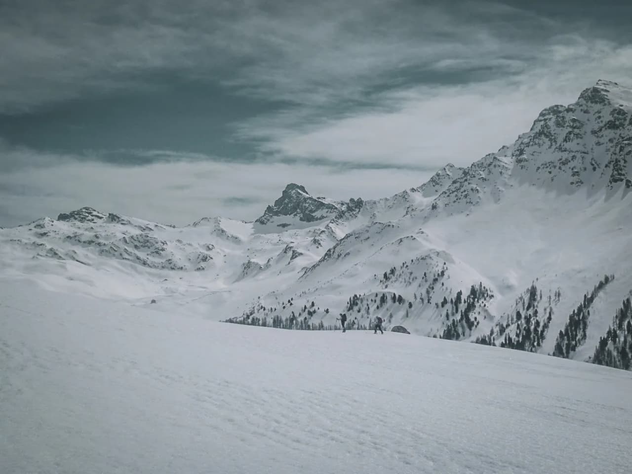 Un paysage alpin époustouflant, avec des sommets enneigés et des aventuriers en ski de randonnée.