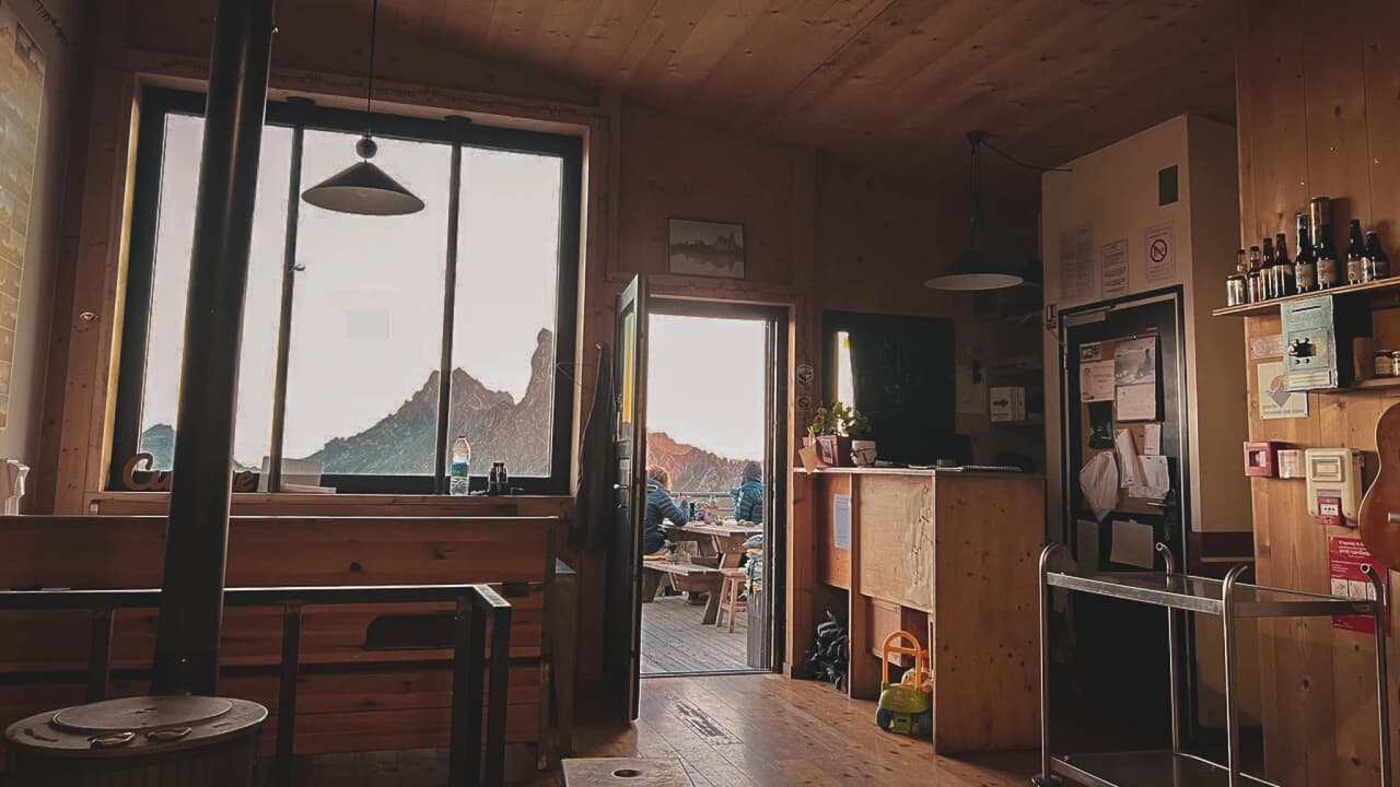 The warm interior of a mountain hut, with views of the peaks and a friendly atmosphere.