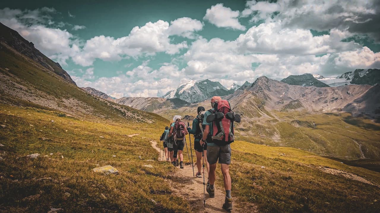 Un groupe de randonneurs traverse un sentier verdoyant avec des montagnes majestueuses en toile de fond.