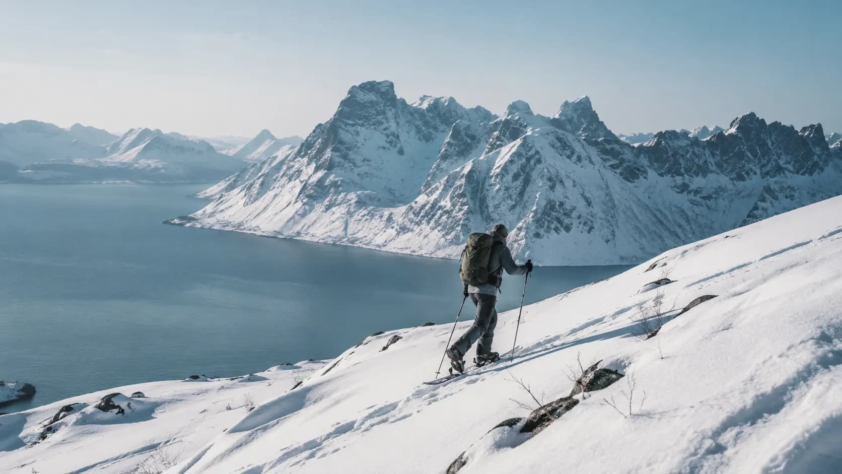 Randonneur en raquettes sur un paysage de fjord enneigé à Senja, Norvège, sous un ciel serein.