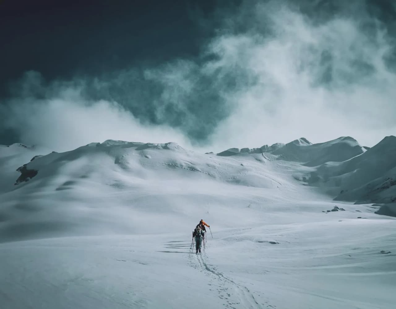 Un aventurier progresse dans un paysage alpin enneigé, sous un ciel tourbillonnant.