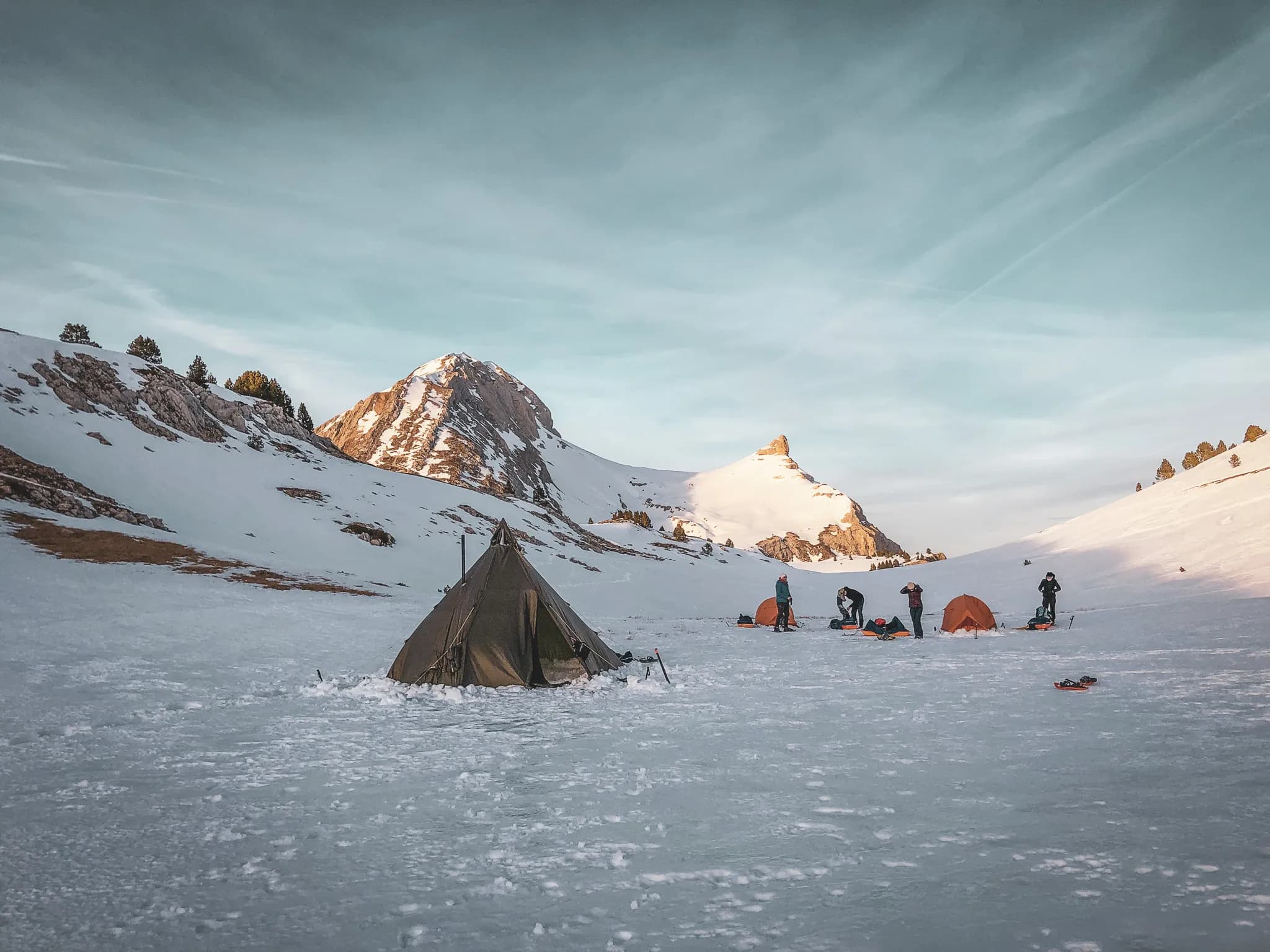 Bivak in de bergen, met tipi's en tenten, onder een heldere hemel en besneeuwde bergtoppen.