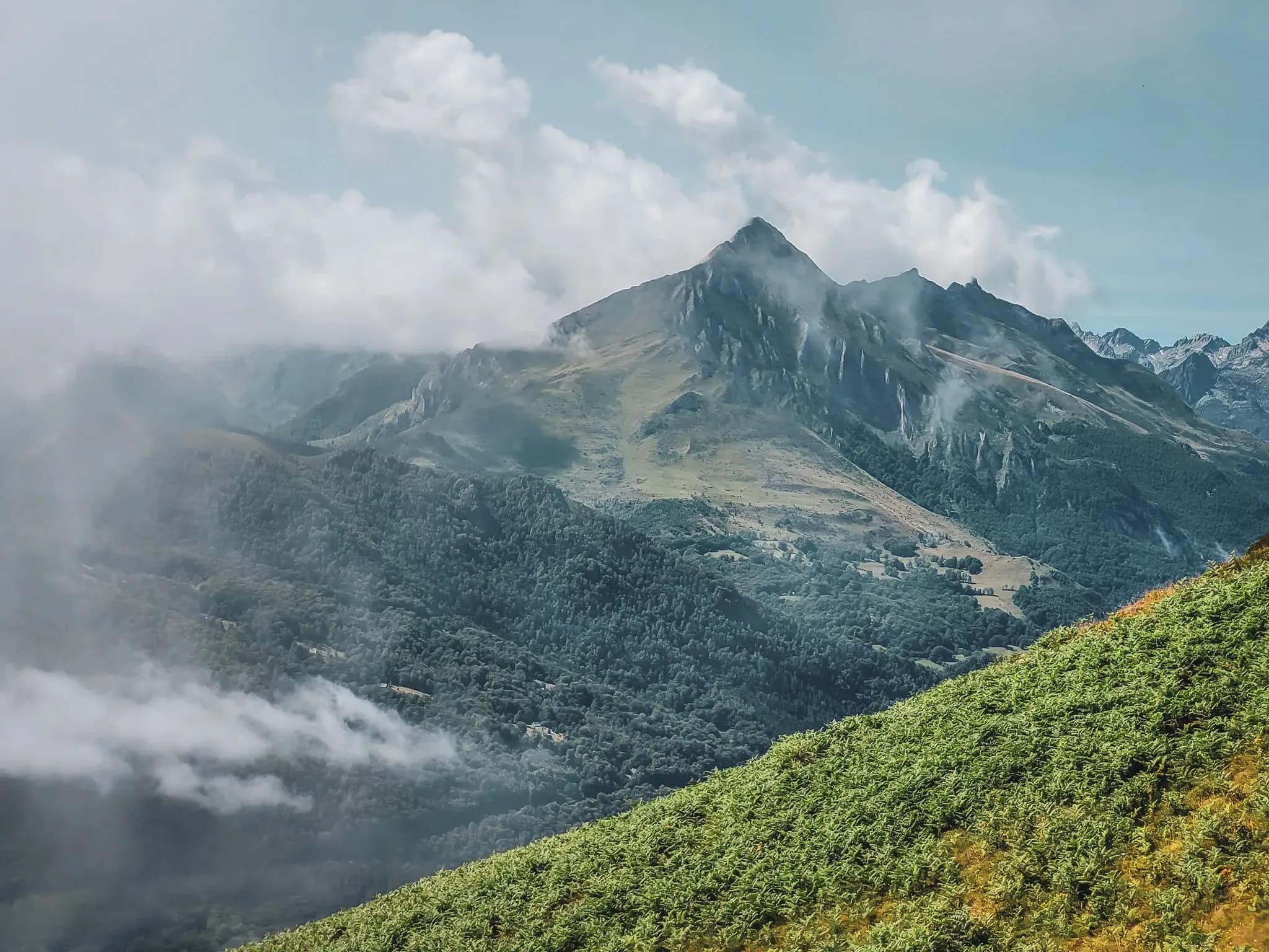 Vue panoramique des montagnes des Pyrénées, embrumées et verdoyantes, invitant à l'aventure.