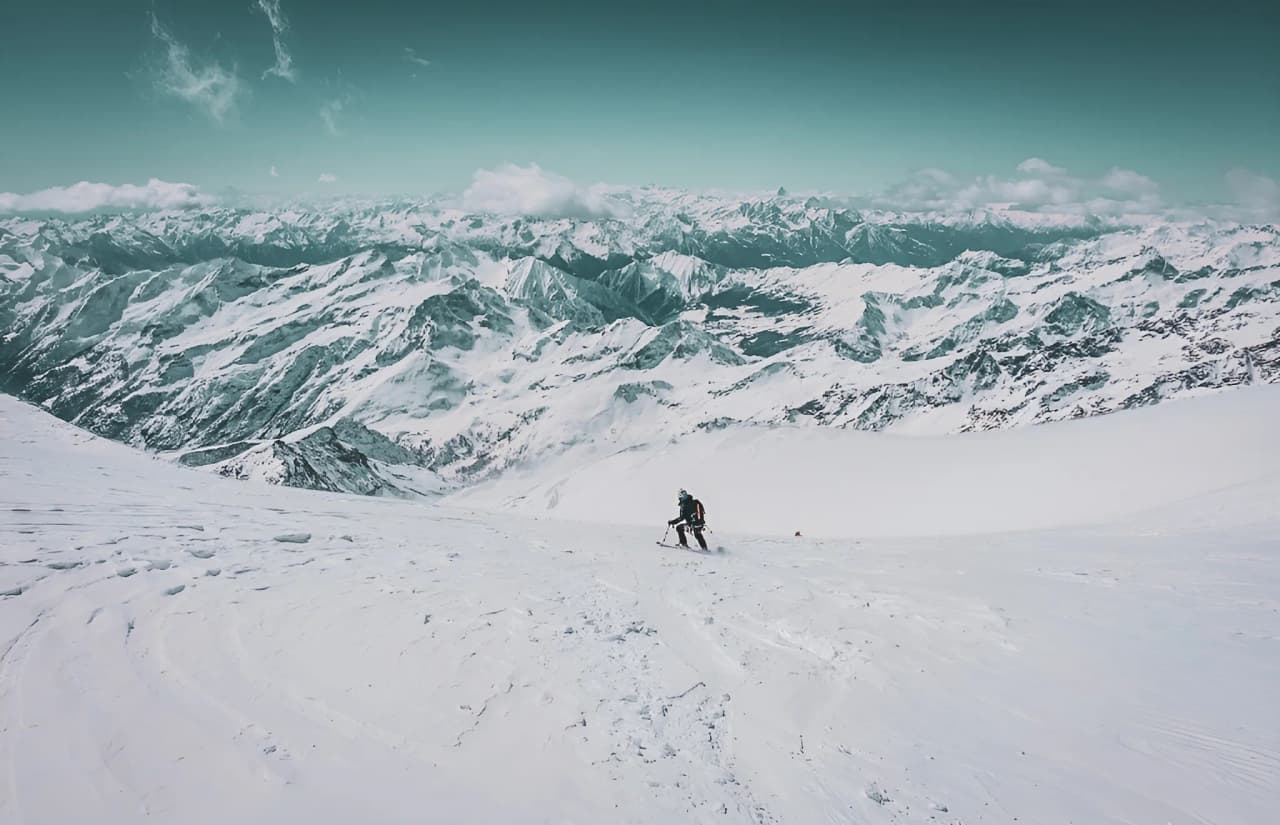 A lone skier on a glacier, surrounded by majestic snow-capped mountains. An alpine adventure.