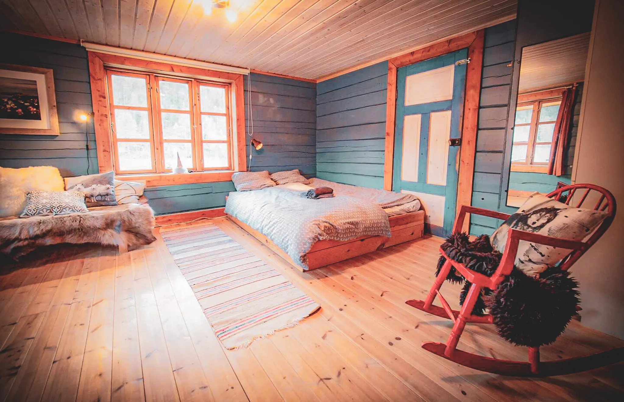 Une chambre accueillante avec des murs en bois peint dans des teintes bleu et beige. Un lit double, recouvert d'une couette à motifs, se trouve au centre, avec deux oreillers sur le dessus. À côté, un petit