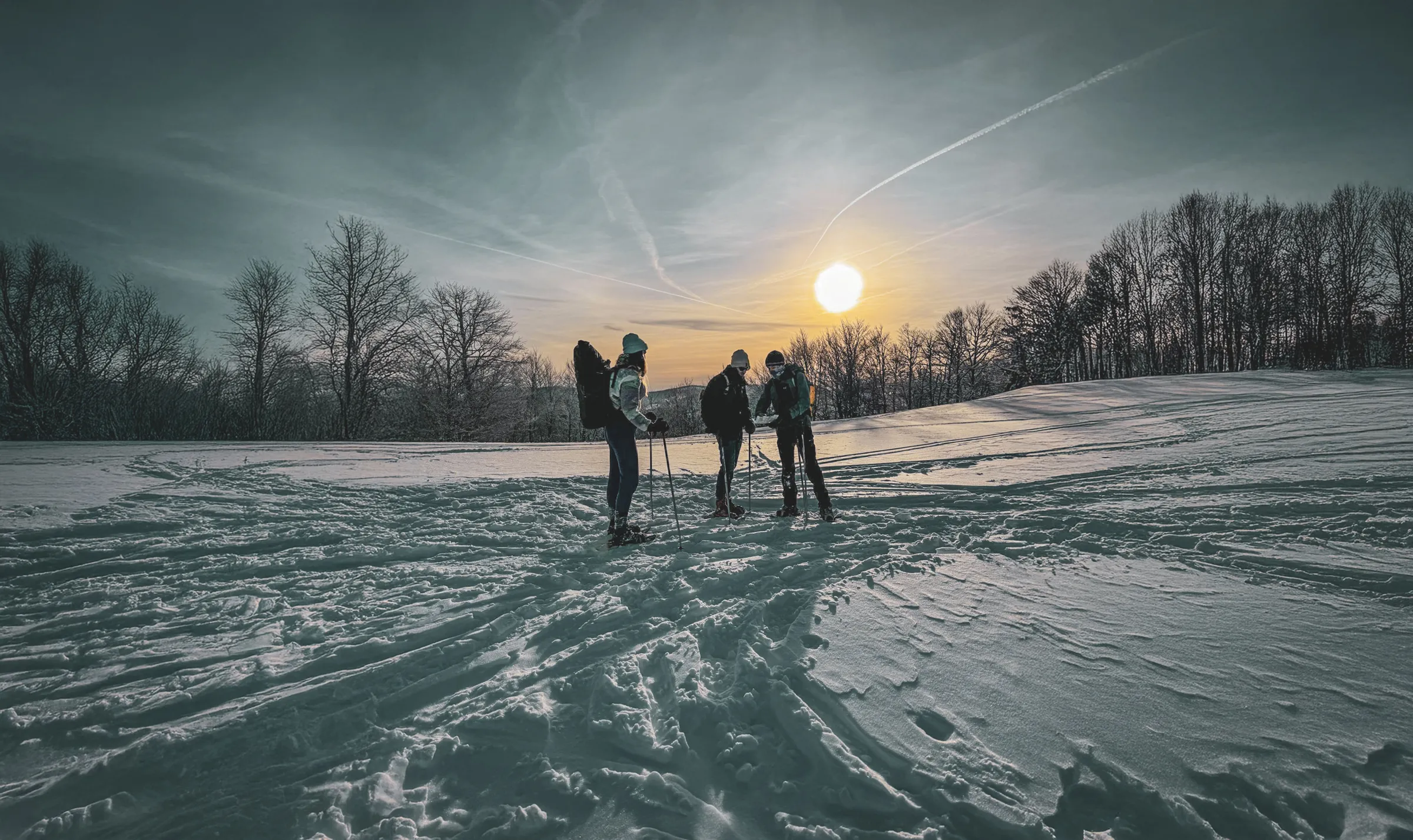 Un groupe de randonneurs en raquettes, sous un ciel d'hiver doré, explore la crête des Vosges enneigée.