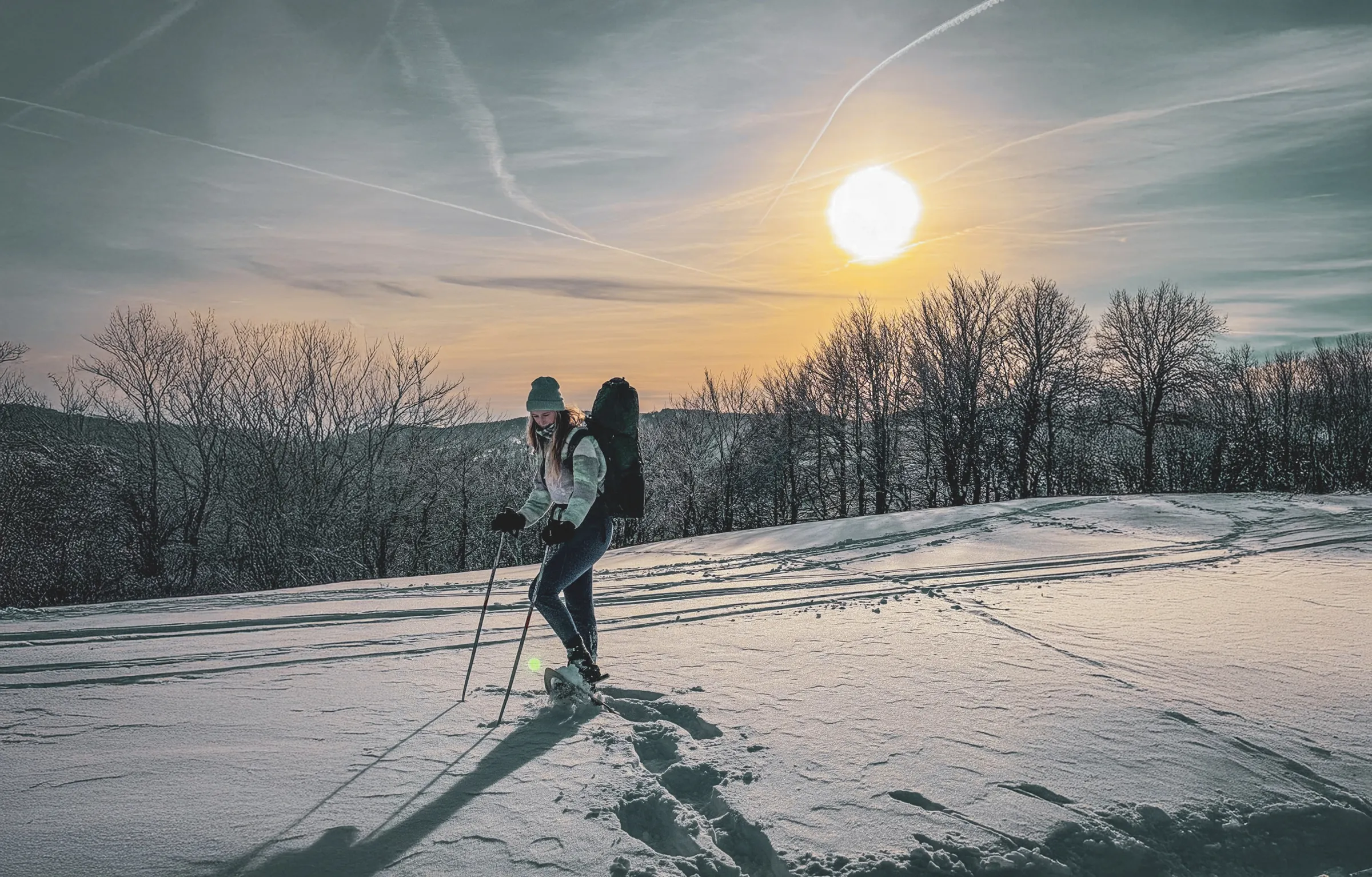 Femme en raquettes sur la crête des Vosges, silhouettée par un coucher de soleil enchanteur.