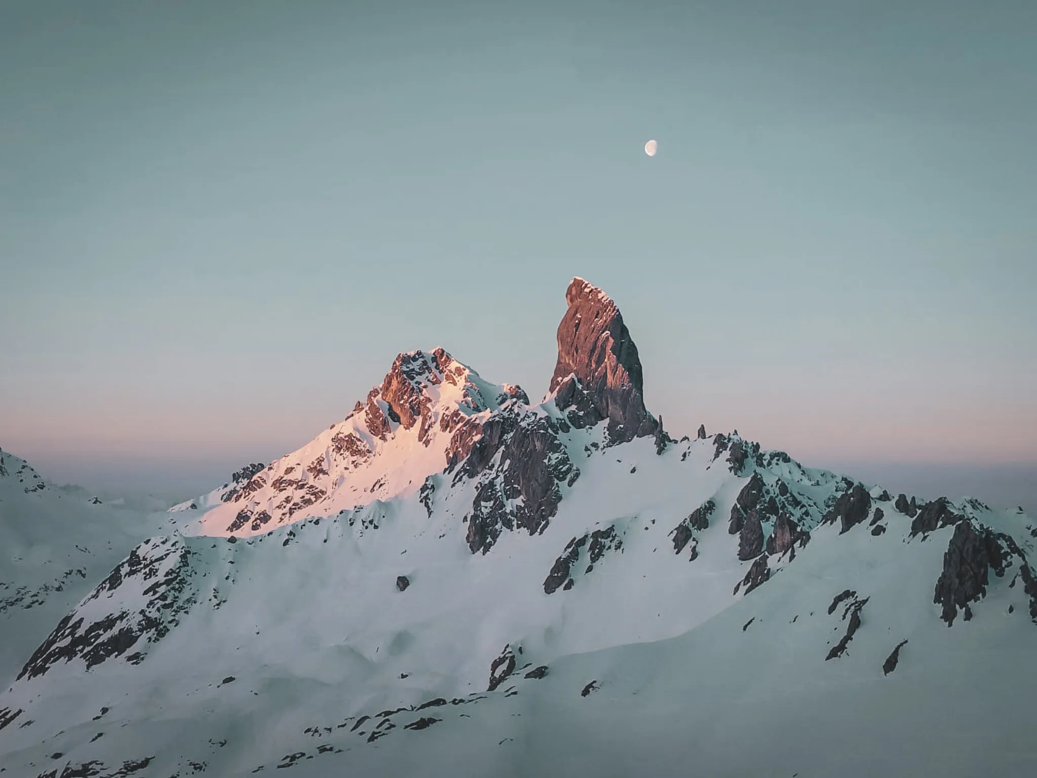 A majestic summit illuminated by the setting sun, surrounded by vast snow-covered landscapes.