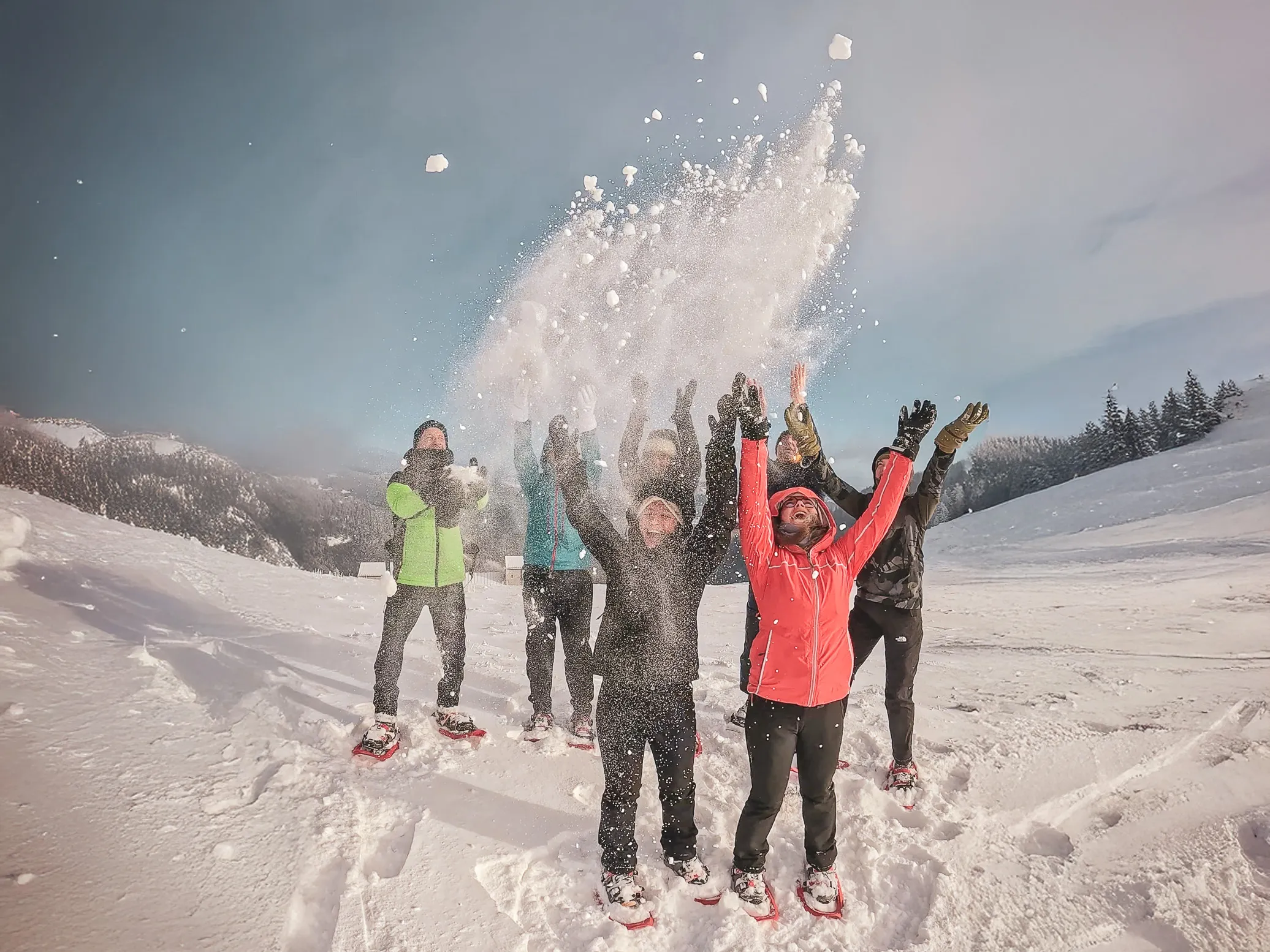 Een enthousiaste groep op sneeuwschoenen, sneeuw aan het gooien onder een zonnige hemel in de Vogezen.