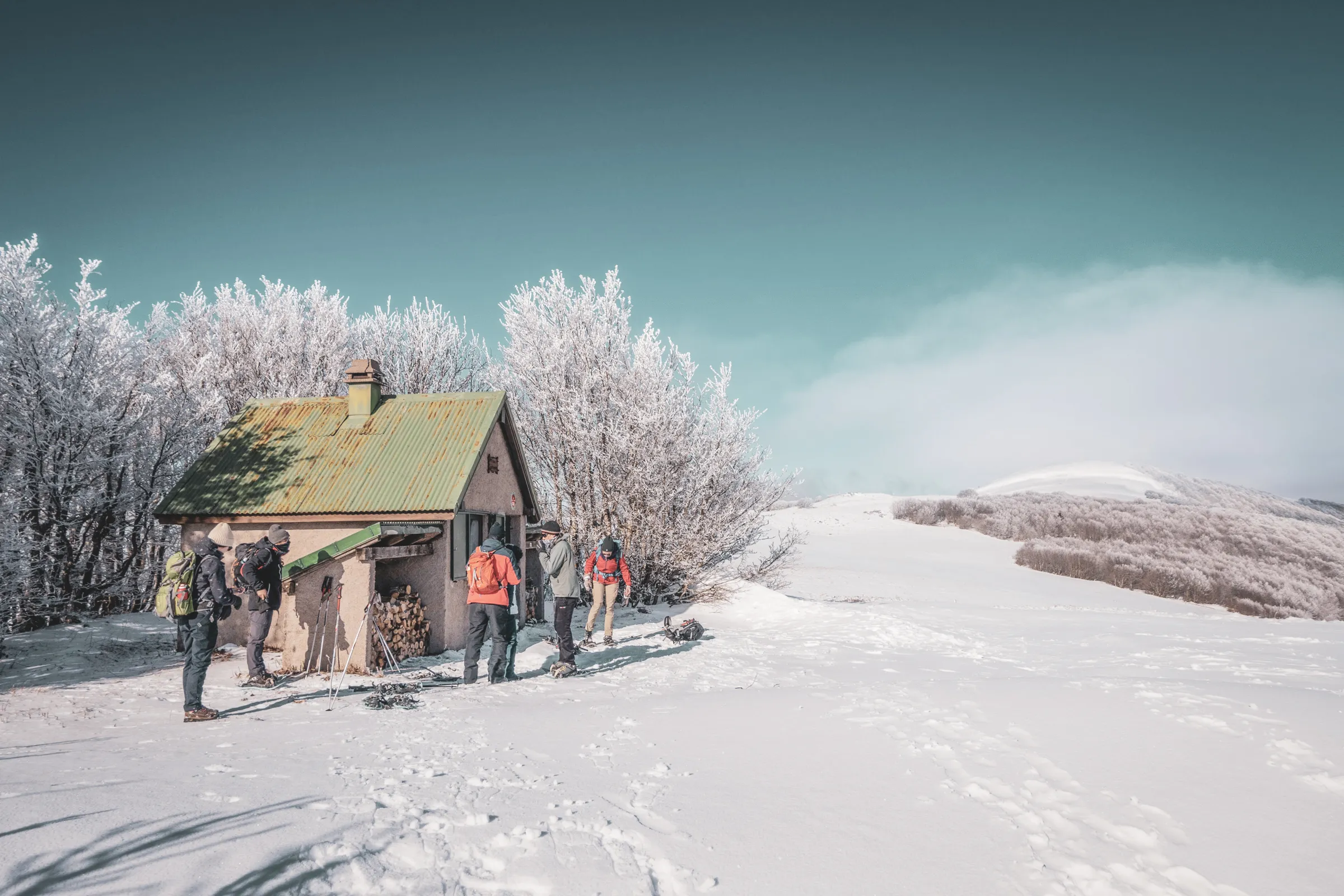Groupe de randonneurs en raquettes, près d'un chalet pittoresque dans un paysage neigeux.