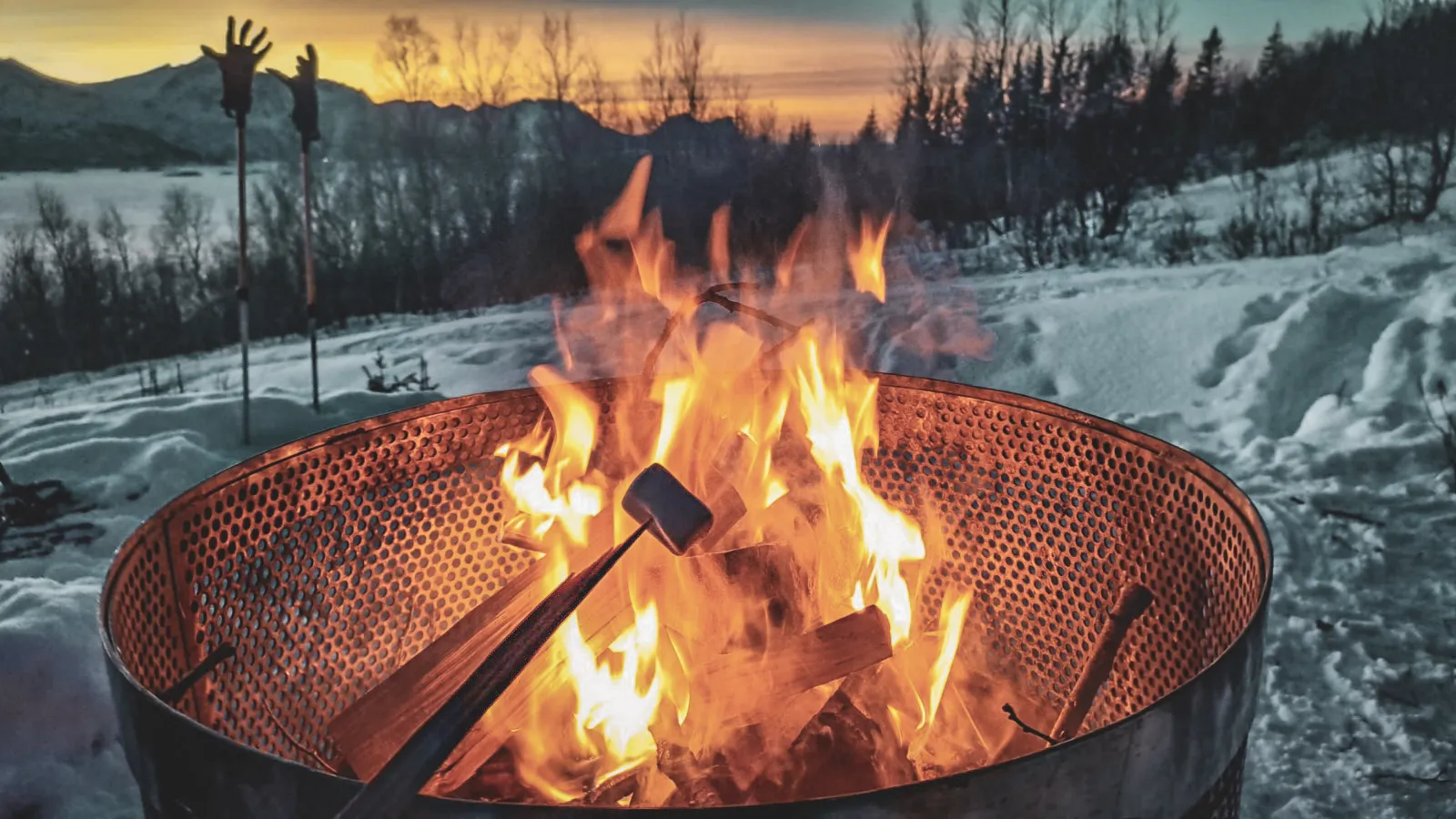 Un feu crépitant au crépuscule, dans un paysage enneigé, idéal pour une soirée cosy en Norvège.