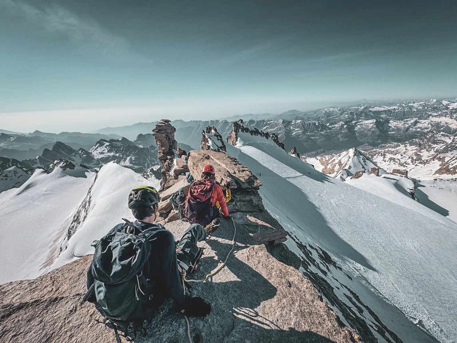 Hikers on an Alpine peak, a breathtaking panorama of snow-capped mountains on the horizon.