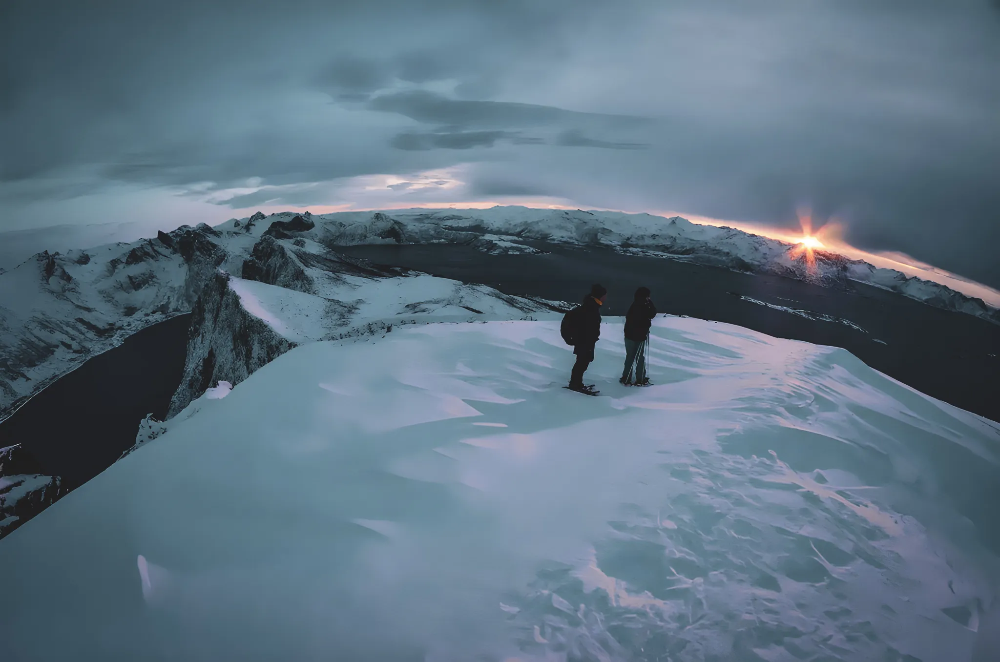 Deux randonneurs admirent un coucher de soleil sur un paysage enneigé des fjords de Senja.