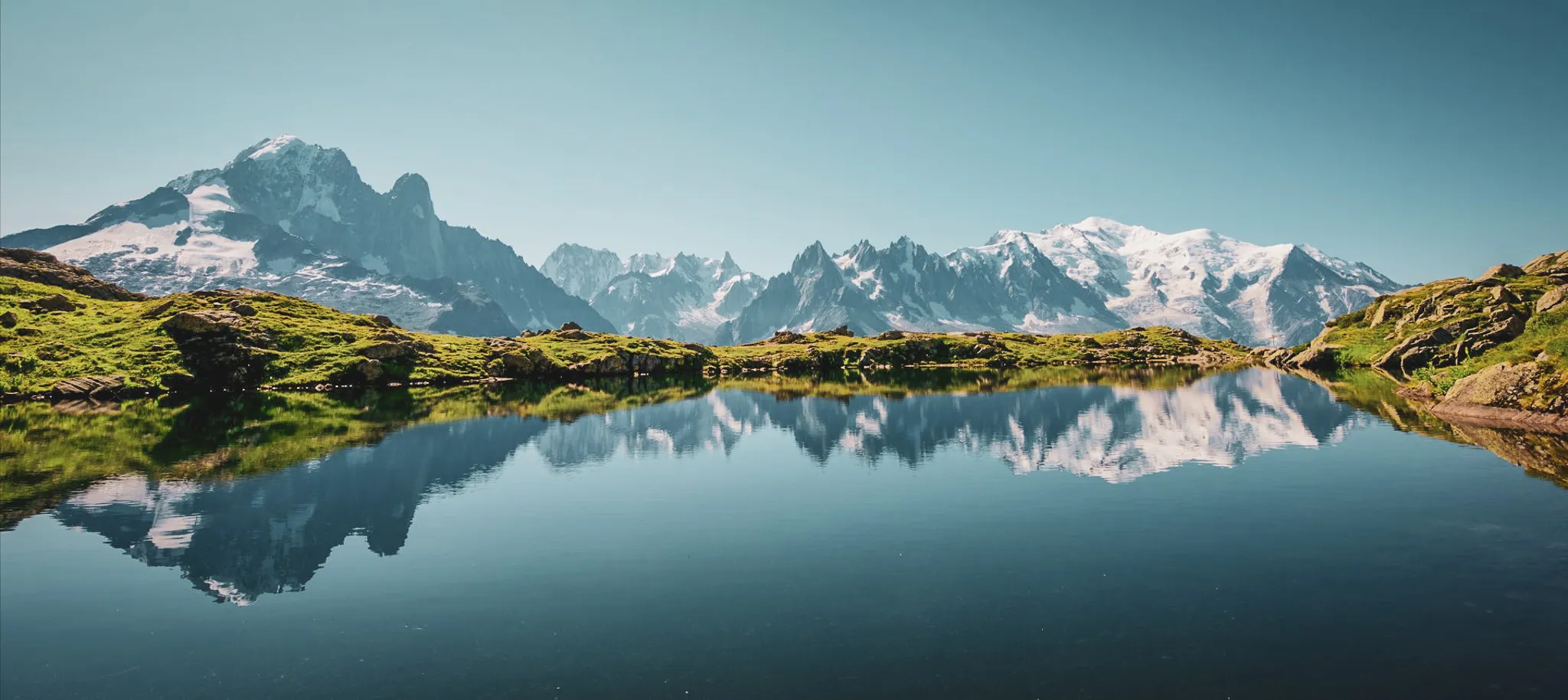 Mirror lake reflecting the majestic Aiguilles Rouges under a radiant blue sky.