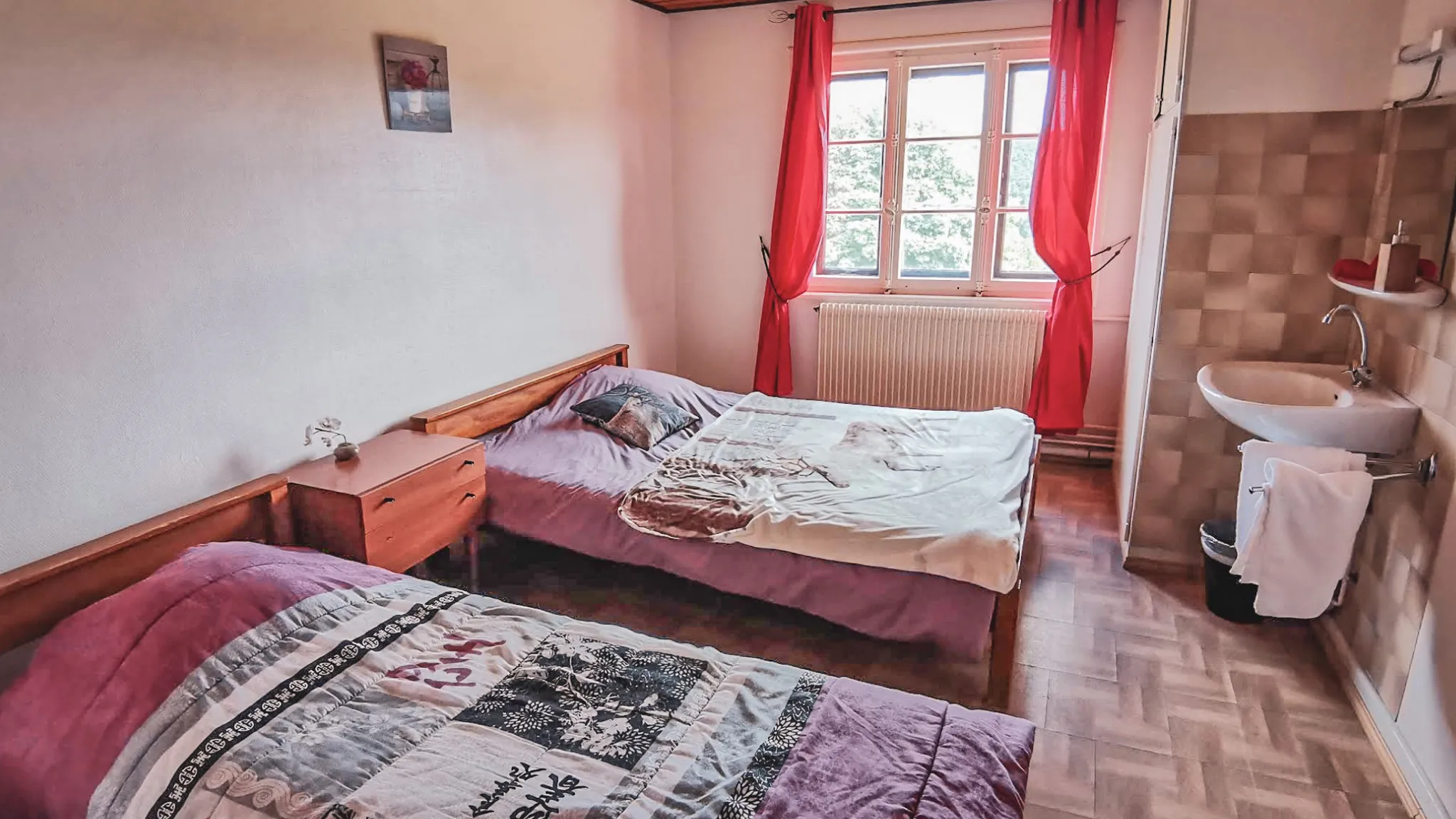 Chambre chaleureuse avec deux lits, fenêtres lumineuses et vue sur la nature vosgienne.