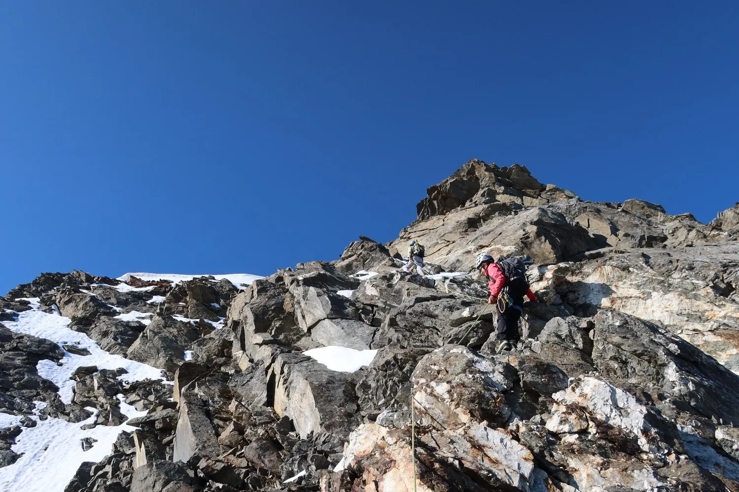 Mountaineers climbing steep rock under a blue sky, facing Mont Blanc. High mountain adventure!