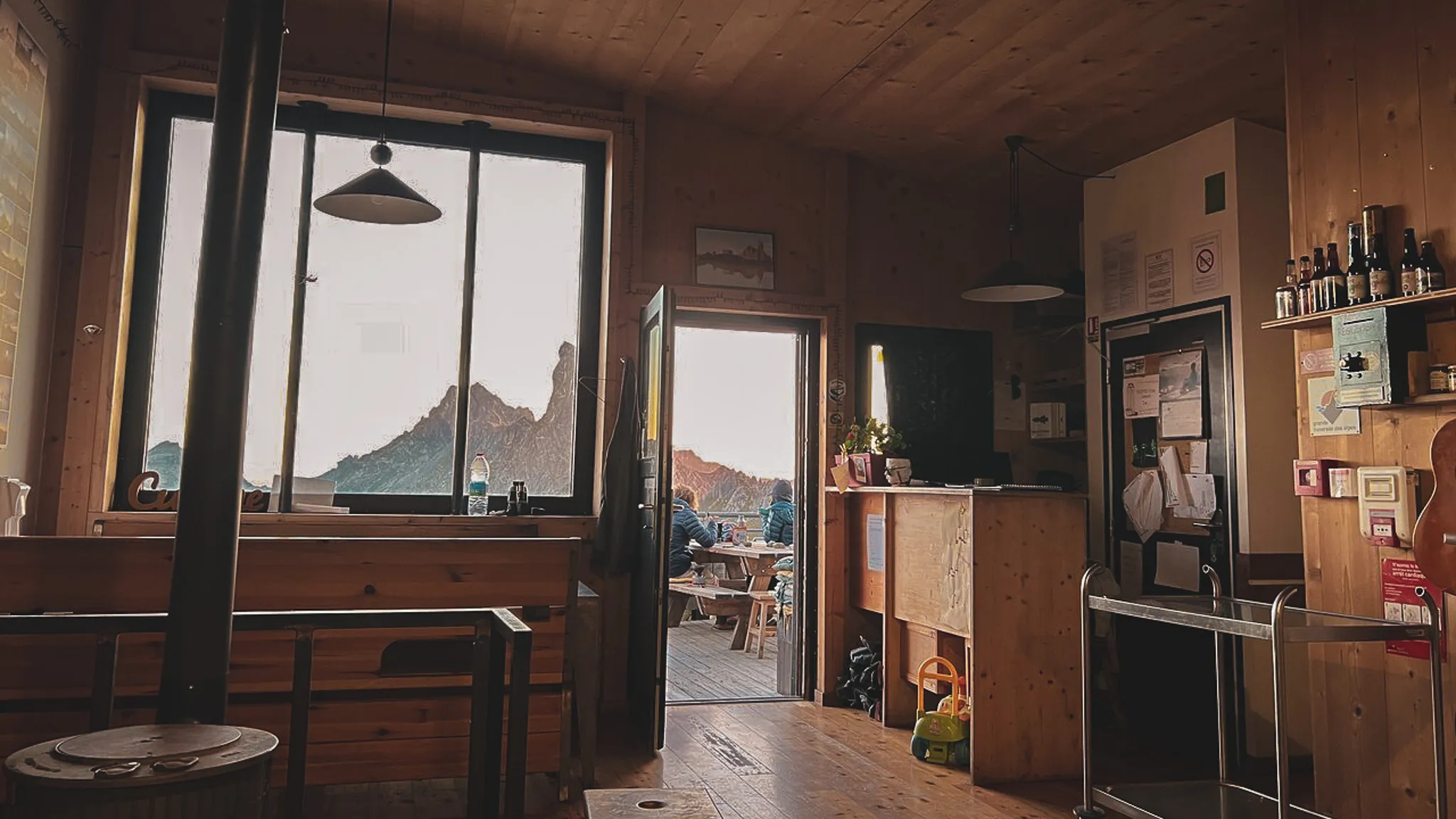 The warm interior of a mountain hut, with views of the peaks and a friendly atmosphere.