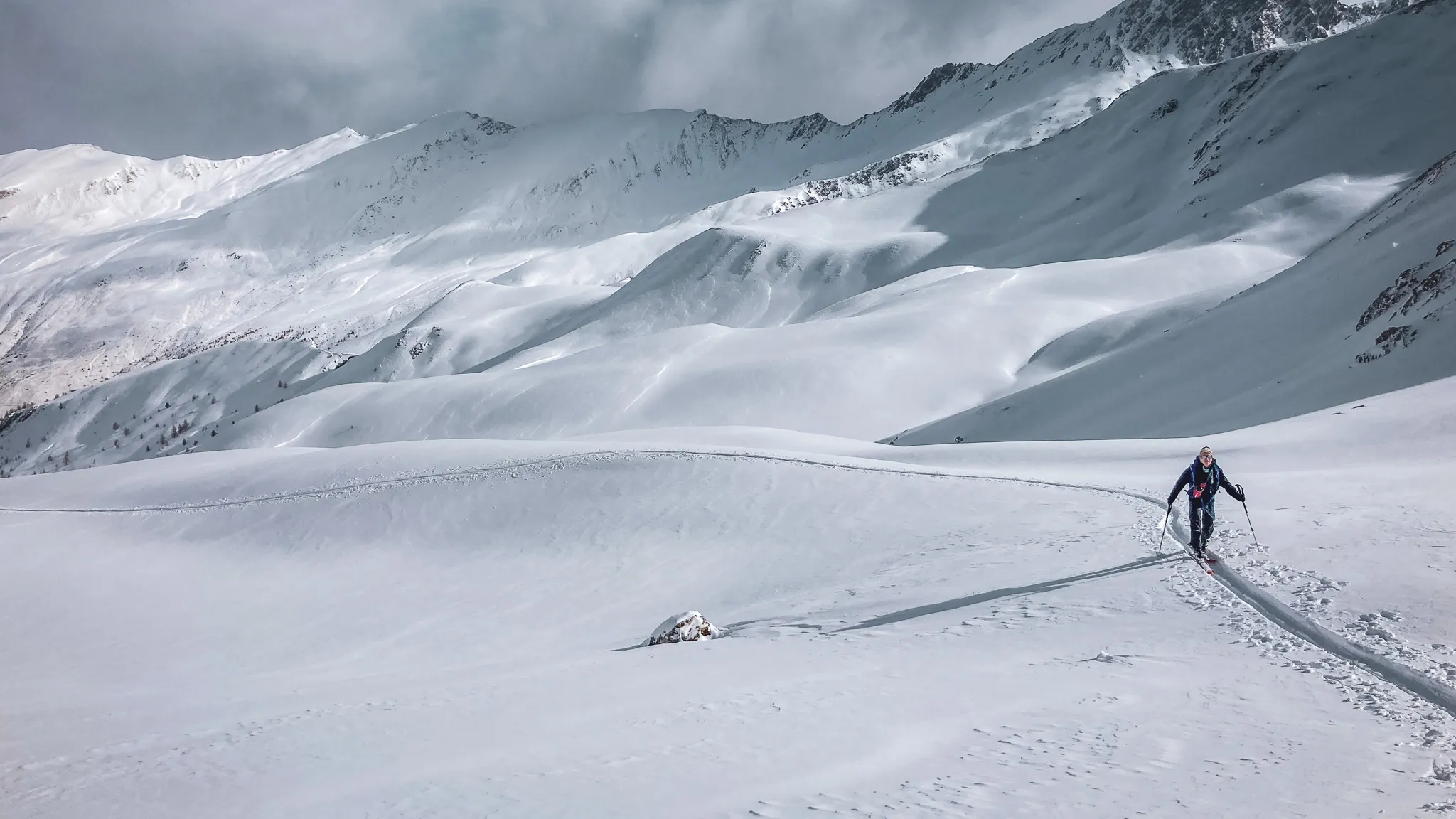 Un skieur solitaire évolue sur un vaste paysage enneigé, dominé par des montagnes majestueuses.