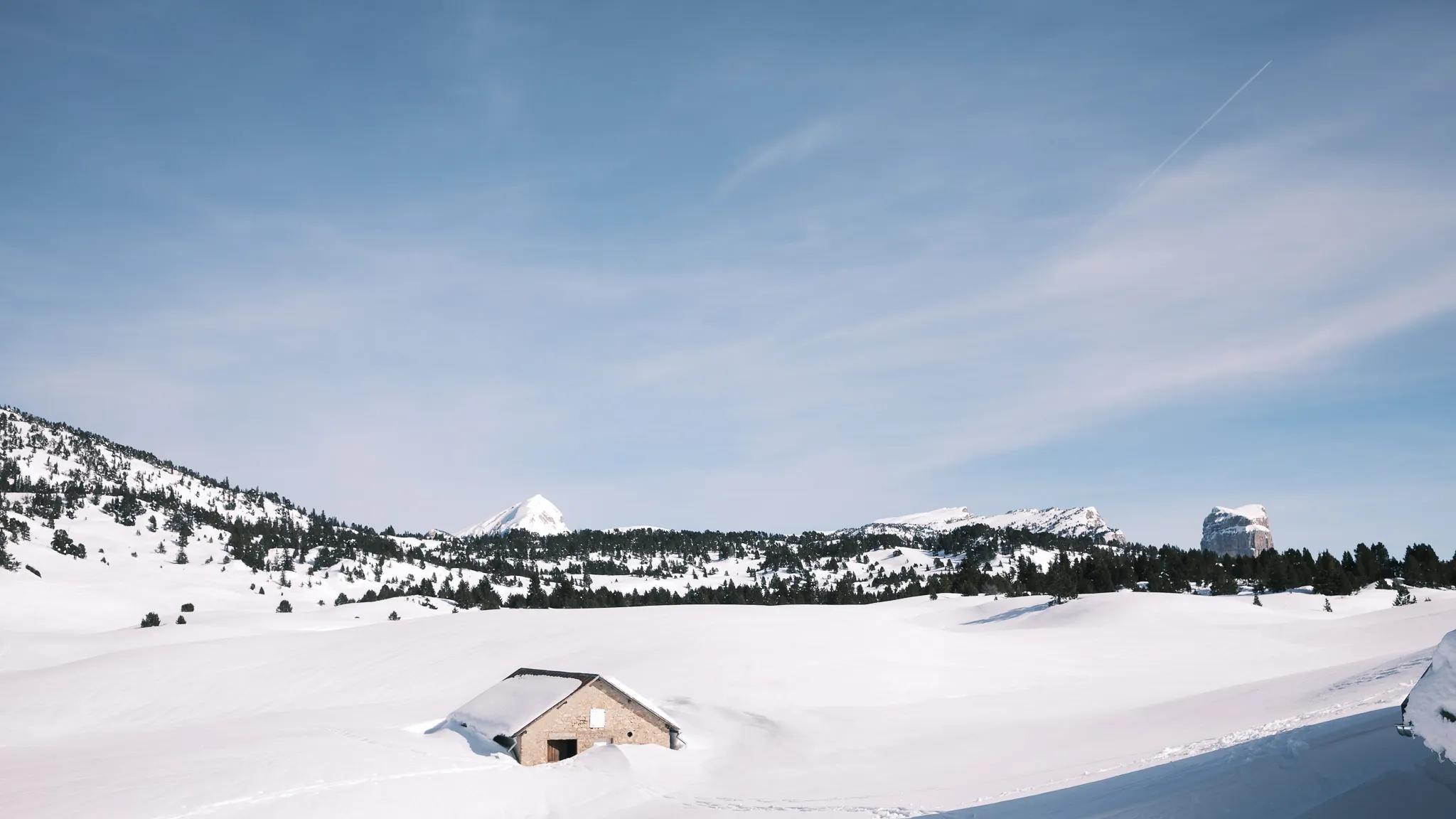 Paysage hivernal du Vercors avec une cabane en pierre, montagnes enneigées et ciel serein.