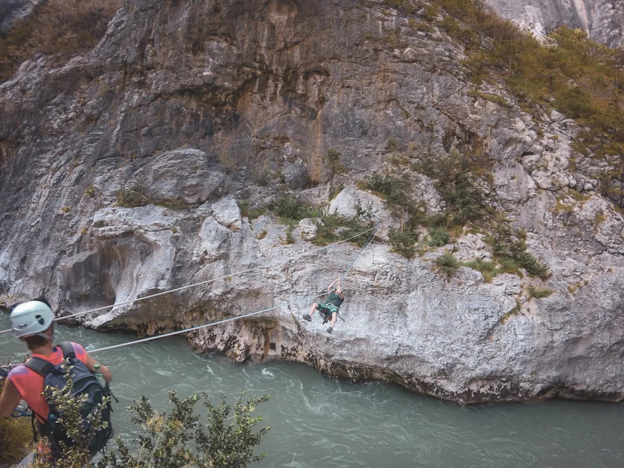 A climber suspended above a river, facing the majestic cliffs of the Gorges du Verdon.