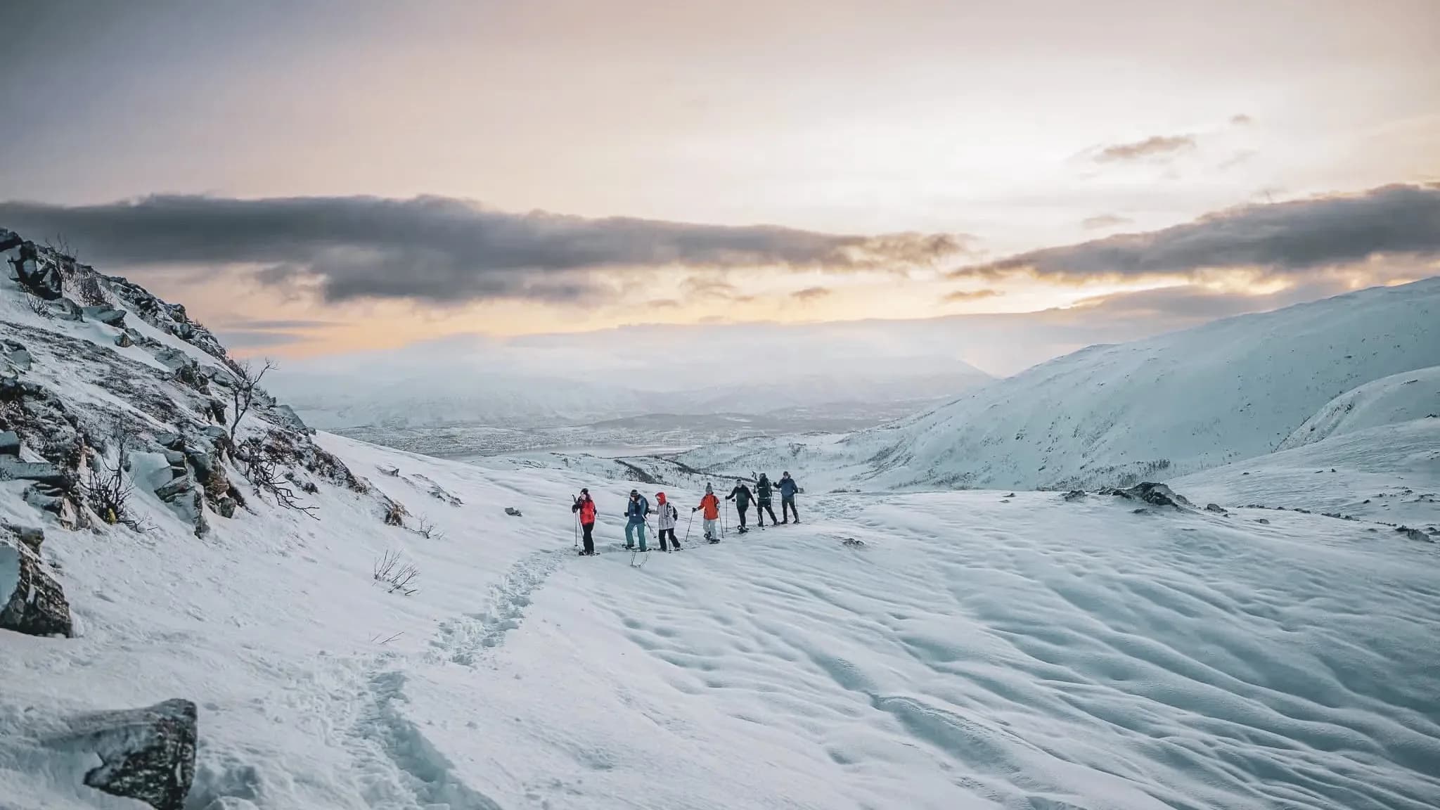 Een groep avonturiers op sneeuwschoenen boven op smetteloze sneeuw, onder een ochtendhemel.