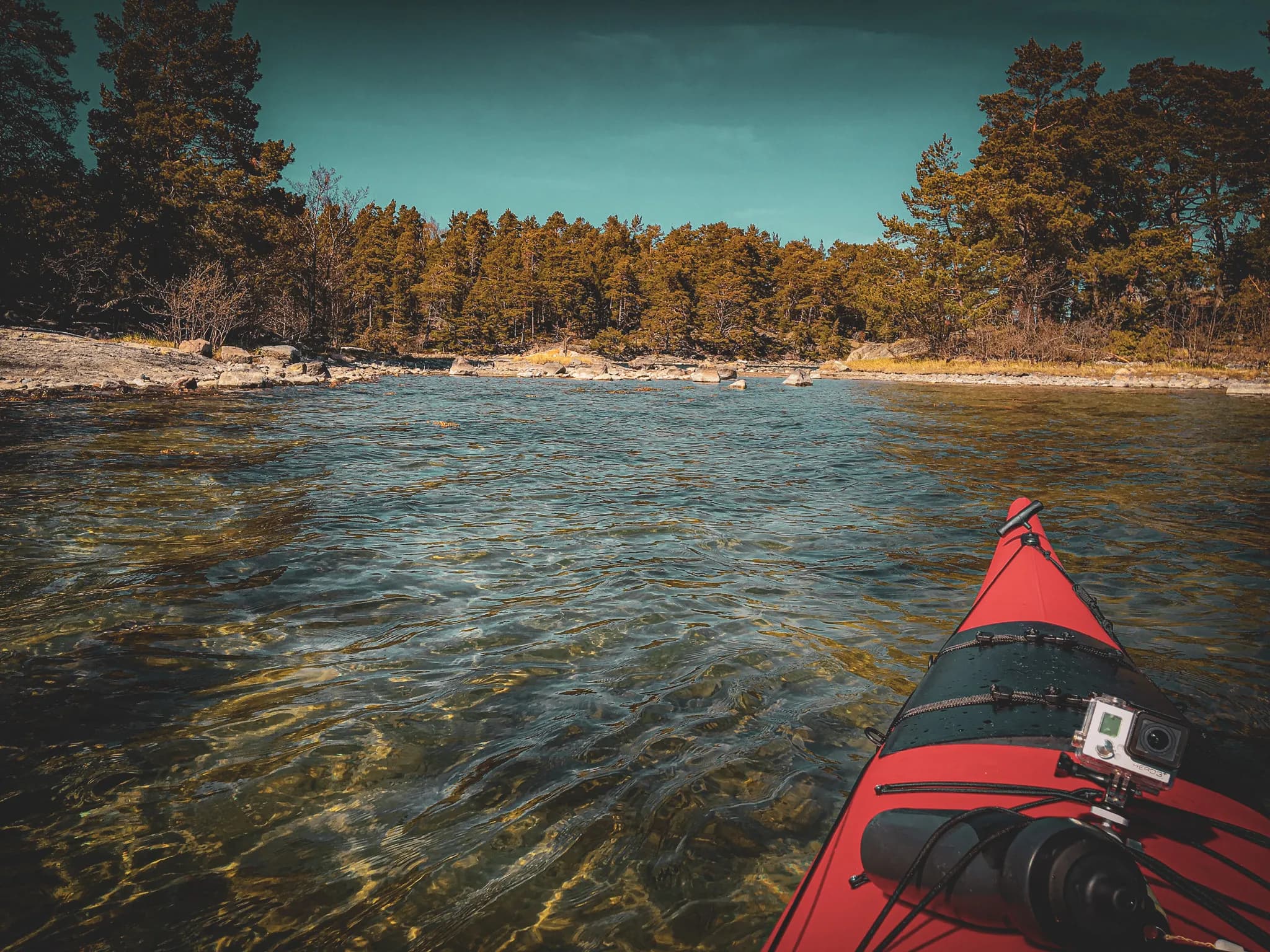 Red kayak in crystal-clear water, surrounded by wild nature, sparkling under the blue sky.