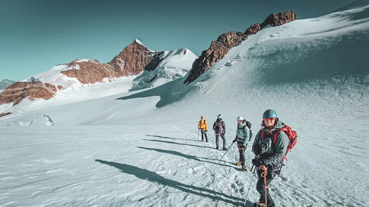 A group of mountaineers on a glacier, with the majestic peaks of Monte Rosa in the background.