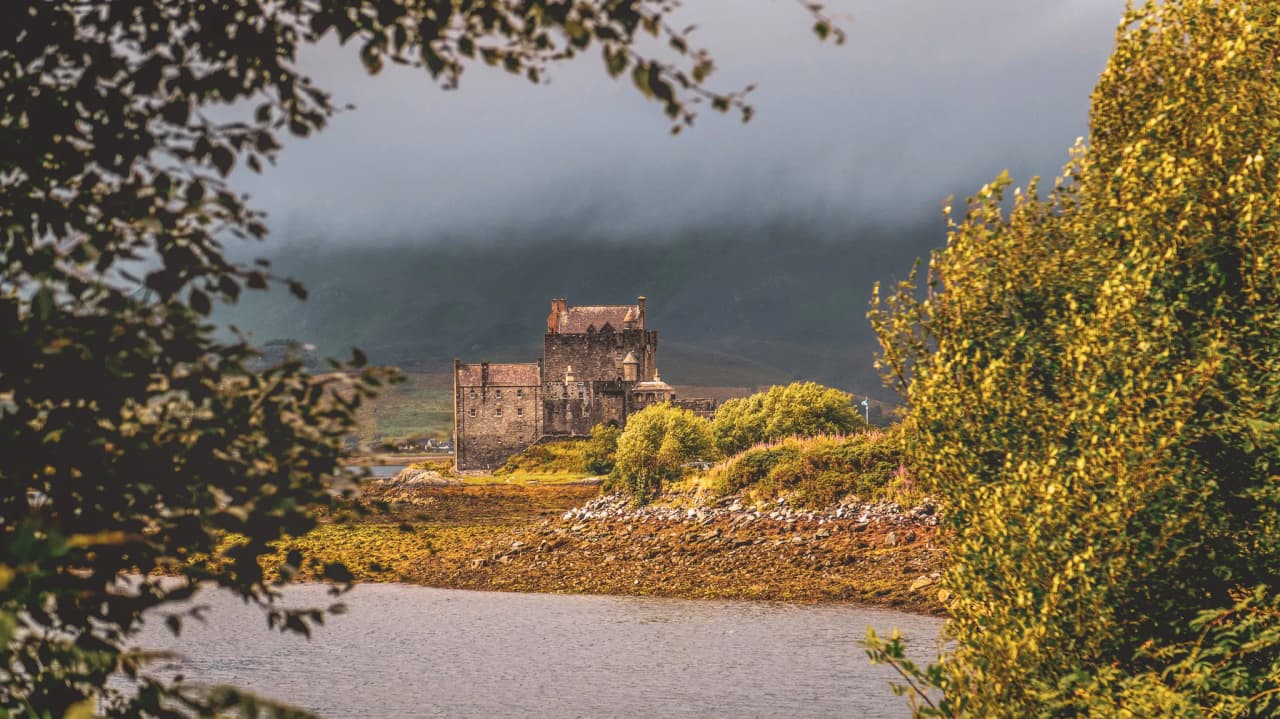 Château pittoresque entouré de verdure, reflet sur un loch, ambiance mystérieuse des Highlands.
